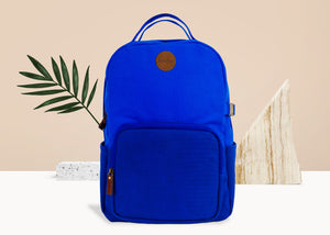 Cobalt blue backpack made from vegan suede and cotton. Features two exterior waterbottle holders, a large front compartment, a rear compartment for a laptop, and a luggage slip. 